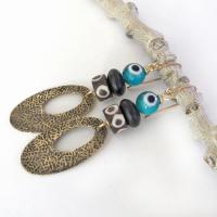 These handmade earrings feature gold brass hoops with a hand stamped texture accented with African batik bone beads and topped off with turquoise color evil eye glass and matte black glass beads.  Evil eye beads are protective amulets designed with concentric circles that mimic the appearance of a human eye. Beads with this symbolism have been used for thousands of years across different cultures to ward off bad luck, illness, or misfortune and push away the negative or envious energy of others.
