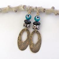 These handmade earrings feature gold brass hoops with a hand stamped texture accented with African batik bone beads and topped off with turquoise color evil eye glass and matte black glass beads.  Evil eye beads are protective amulets designed with concentric circles that mimic the appearance of a human eye. Beads with this symbolism have been used for thousands of years across different cultures to ward off bad luck, illness, or misfortune and push away the negative or envious energy of others.