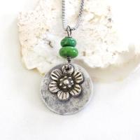 This handmade necklace features a silver tone pewter flower charm framed against an aluminum circle accented with a stack of natural green serpentine gemstones. It comes on a 20" stainless steel chain necklace with lobster claw closure. It'll make a great gift for anyone that loves flowers or nature.
