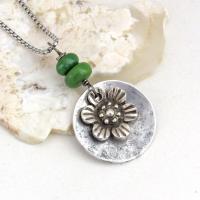 This handmade necklace features a silver tone pewter flower charm framed against an aluminum circle accented with a stack of natural green serpentine gemstones. It comes on a 20" stainless steel chain necklace with lobster claw closure. It'll make a great gift for anyone that loves flowers or nature.