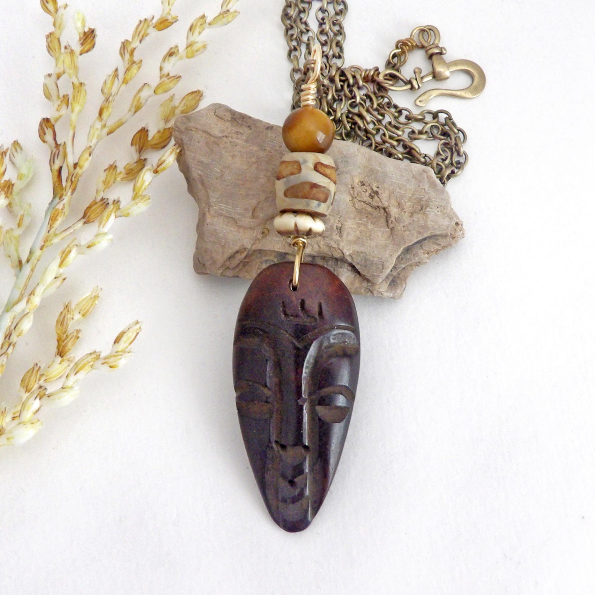 This handcrafted necklace features a carved wood African mask accented with a giraffe print etched agate, golden tiger's eye gemstones and an African carved bone bead. Unique and striking, it'll make a great gift for someone that loves one-of-a-kind ethnic inspired jewelry! It comes on an 18” antiqued brass chain with sturdy hook & eye closure.  Makes a great gift for a man or women that loves African art!           