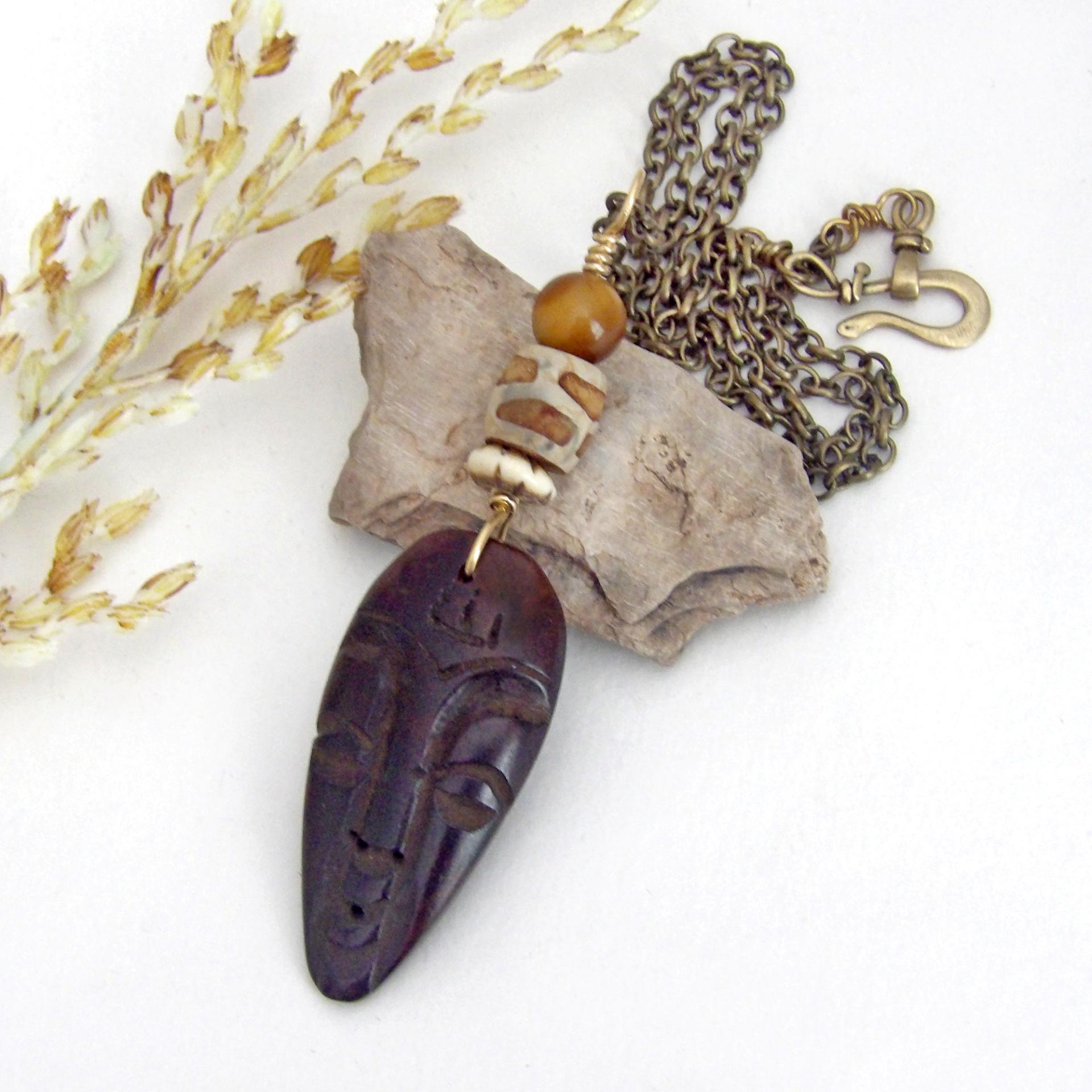 This handcrafted necklace features a carved wood African mask accented with a giraffe print etched agate, golden tiger's eye gemstones and an African carved bone bead. Unique and striking, it'll make a great gift for someone that loves one-of-a-kind ethnic inspired jewelry! It comes on an 18” antiqued brass chain with sturdy hook & eye closure.  Makes a great gift for a man or women that loves African art!