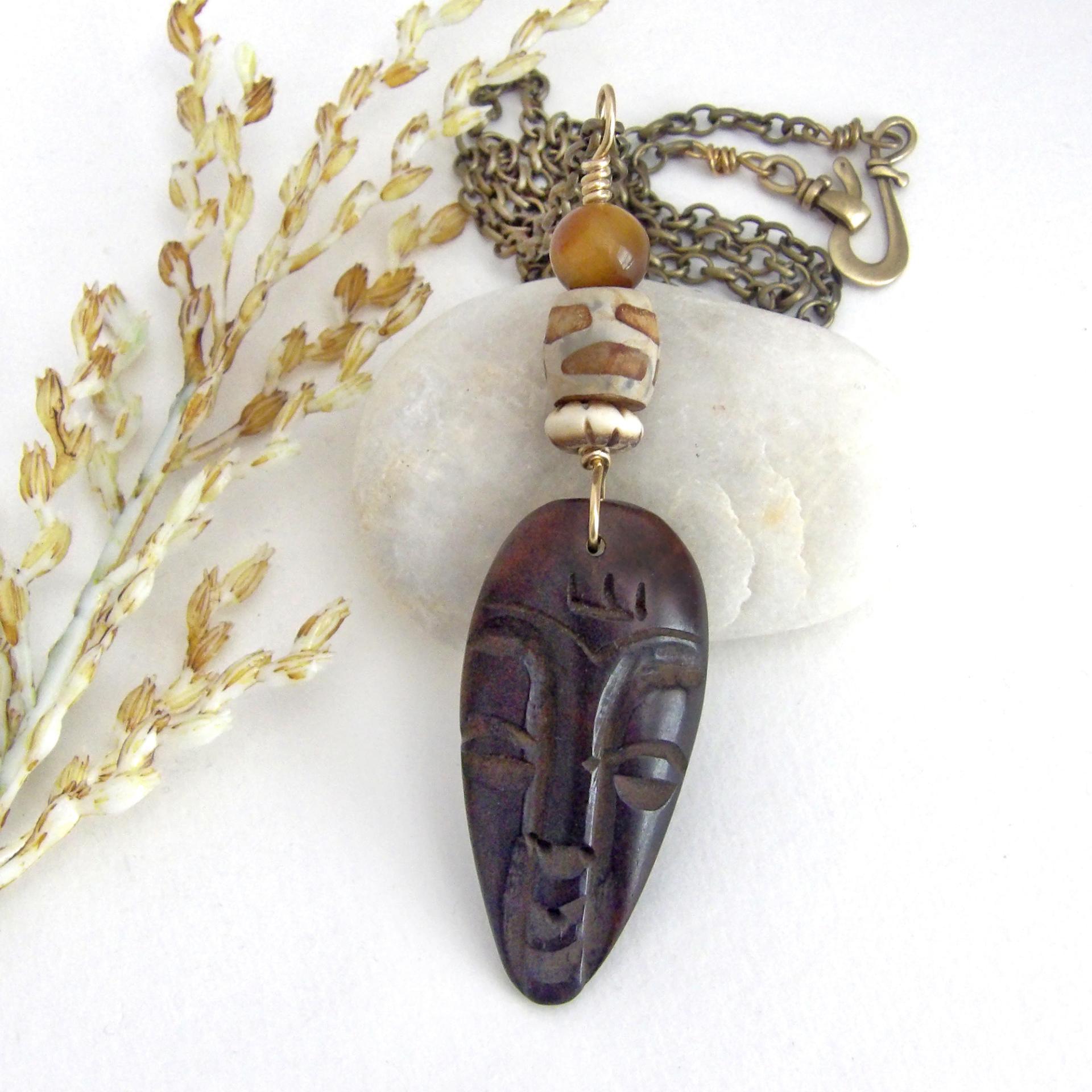 This handcrafted necklace features a carved wood African mask accented with a giraffe print etched agate, golden tiger's eye gemstones and an African carved bone bead. Unique and striking, it'll make a great gift for someone that loves one-of-a-kind ethnic inspired jewelry! It comes on an 18” antiqued brass chain with sturdy hook & eye closure.  Makes a great gift for a man or women that loves African art!