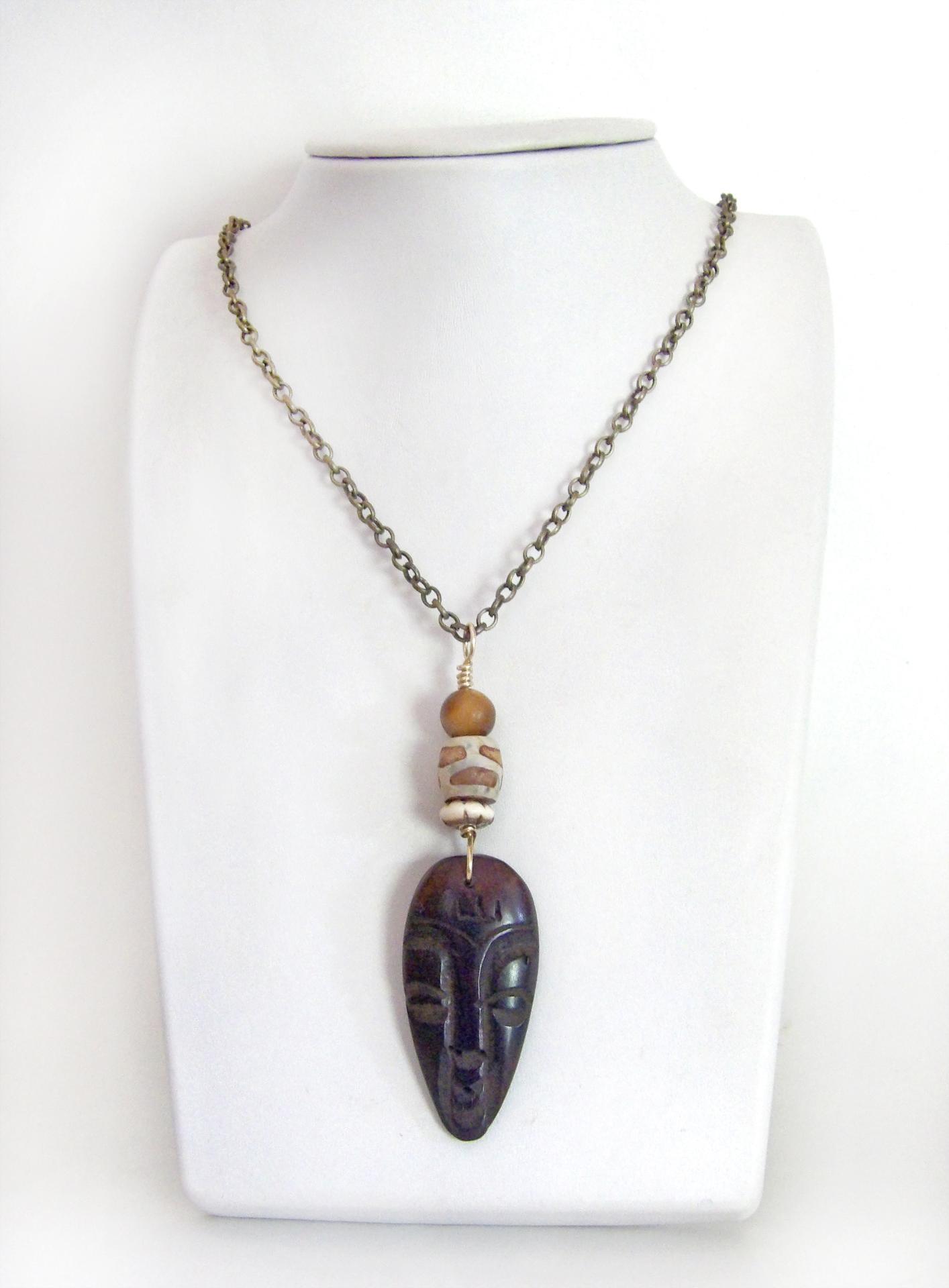 This handcrafted necklace features a carved wood African mask accented with a giraffe print etched agate, golden tiger's eye gemstones and an African carved bone bead. Unique and striking, it'll make a great gift for someone that loves one-of-a-kind ethnic inspired jewelry! It comes on an 18” antiqued brass chain with sturdy hook & eye closure.  Makes a great gift for a man or women that loves African art!