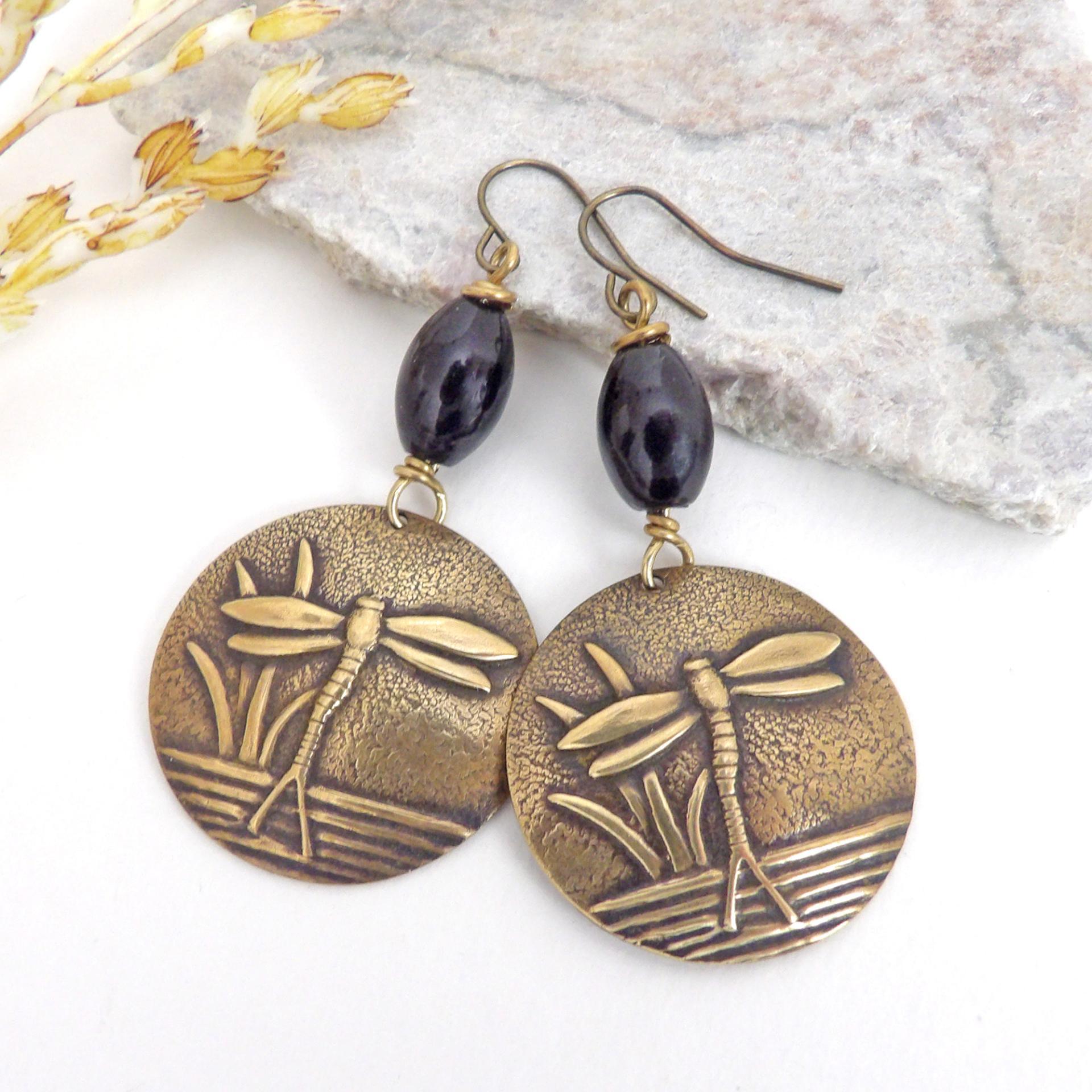 These handmade earrings feature gold brass charms with an embossed nature pattern of dragonflies and leaves. They are accented with black beads and dangle from antiqued brass ear wires. Lightweight and comfortable to wear, they'll make a great gift for a nature lover.