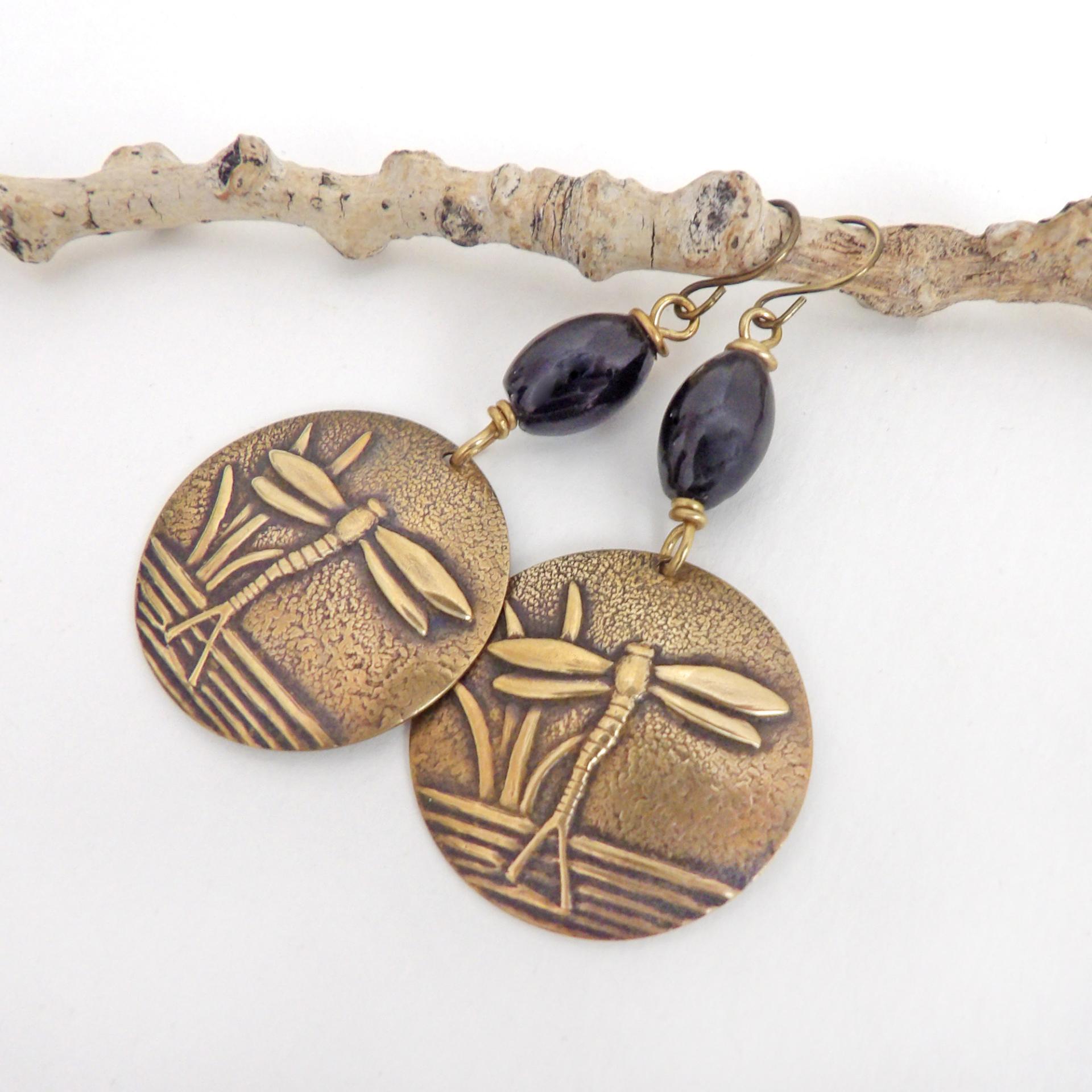 These handmade earrings feature gold brass charms with an embossed nature pattern of dragonflies and leaves. They are accented with black beads and dangle from antiqued brass ear wires. Lightweight and comfortable to wear, they'll make a great gift for a nature lover.