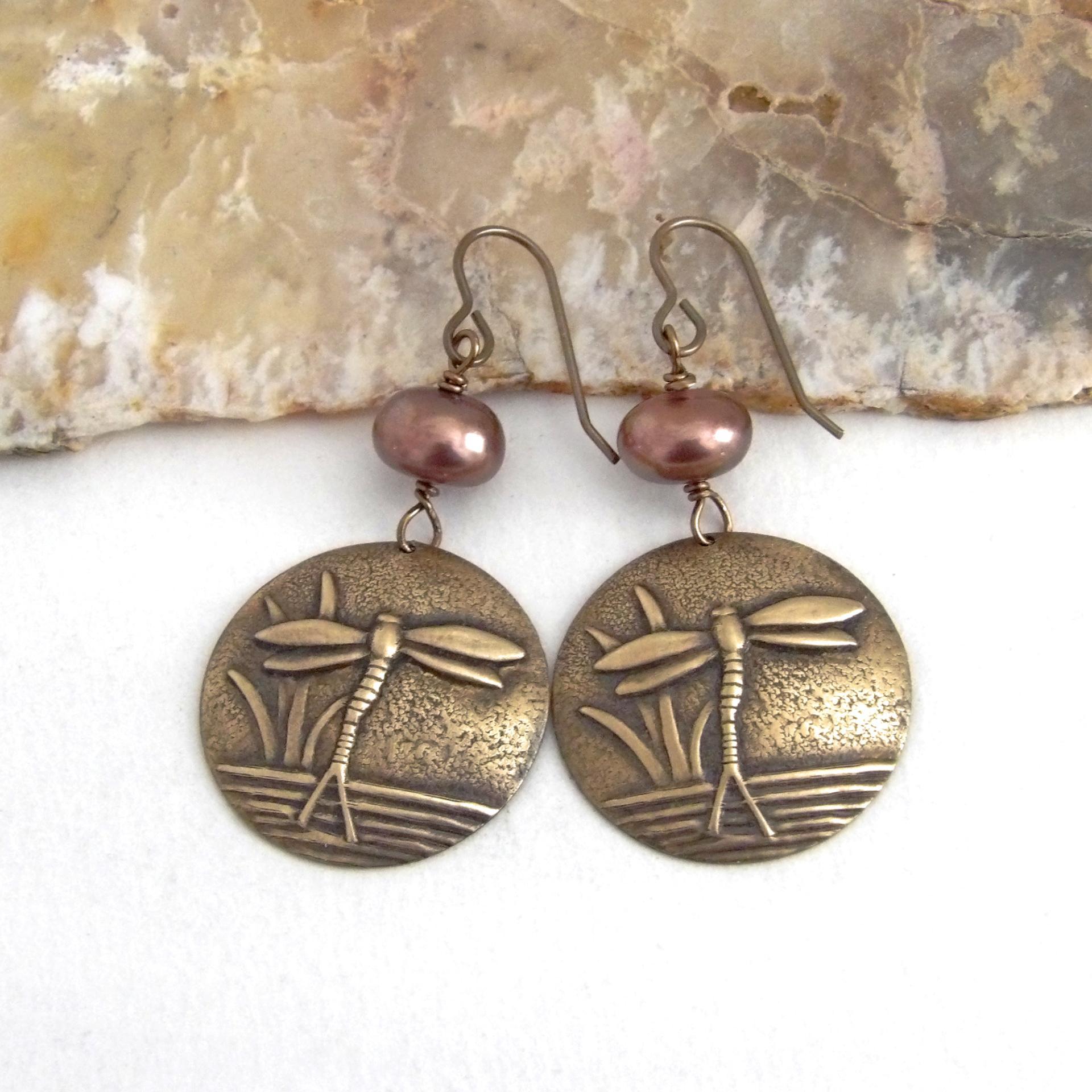 These handmade earrings feature antiqued gold brass charms with an embossed nature pattern of dragonflies and leaves. They are accented with bronze freshwater pearls and dangle from antiqued brass ear wires. Lightweight and comfortable to wear, they'll make a great gift for a nature lover.