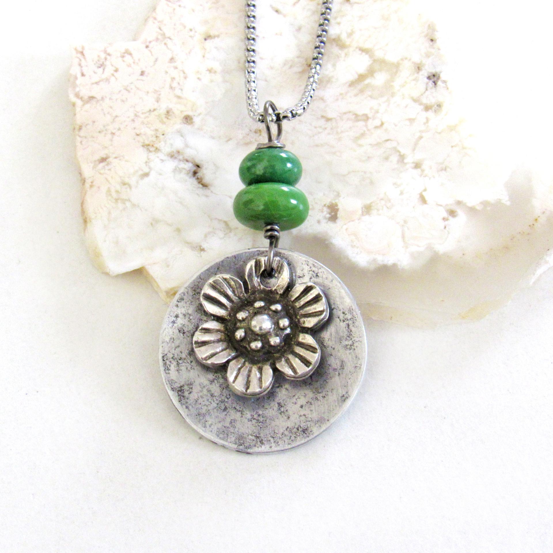 This handmade necklace features a silver tone pewter flower charm framed against an aluminum circle accented with a stack of natural green serpentine gemstones. It comes on a 20" stainless steel chain necklace with lobster claw closure. It'll make a great gift for anyone that loves flowers or nature.