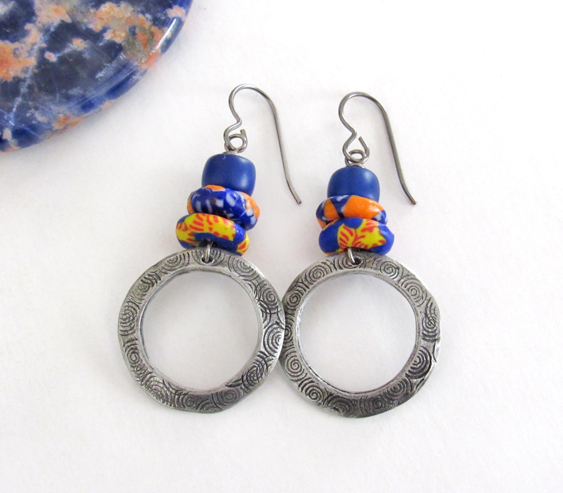 These handcrafted earrings feature silver pewter circle hoops with a hand stamped texture accented with colorful African glass beads and navy blue glass beads. They have an earthy, boho style and are lightweight and comfortable to wear.  MEASUREMENTS: Total length 2" from top of gray silver niobium (hypoallergenic) ear wires and 1” at widest point. The circles were created out of solid lead-free pewter; hand stamped and oxidized; and signed on the back with my initials