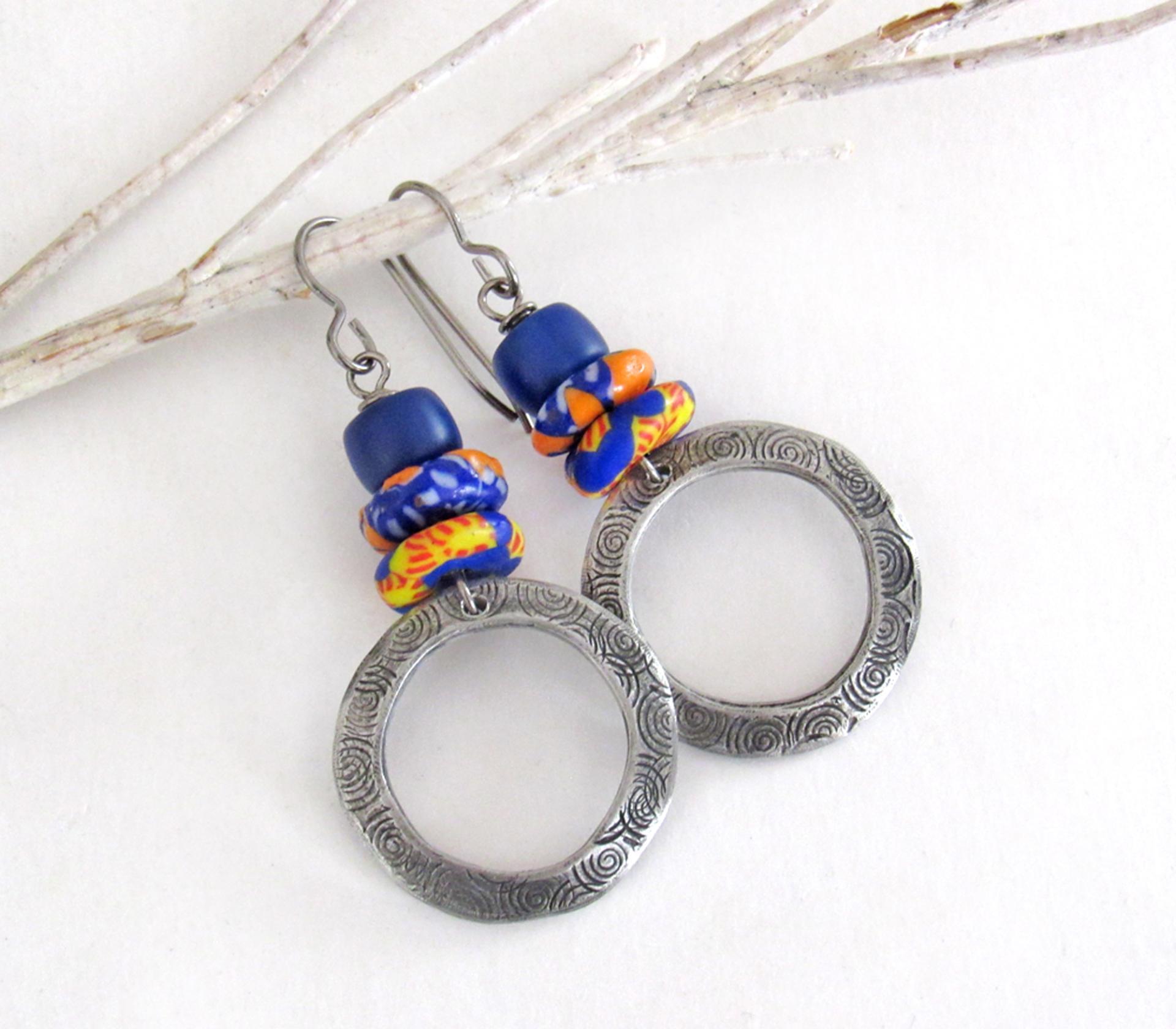 These handcrafted earrings feature silver pewter circle hoops with a hand stamped texture accented with colorful African glass beads and navy blue glass beads. They have an earthy, boho style and are lightweight and comfortable to wear.  MEASUREMENTS: Total length 2" from top of gray silver niobium (hypoallergenic) ear wires and 1” at widest point. The circles were created out of solid lead-free pewter; hand stamped and oxidized; and signed on the back with my initials
