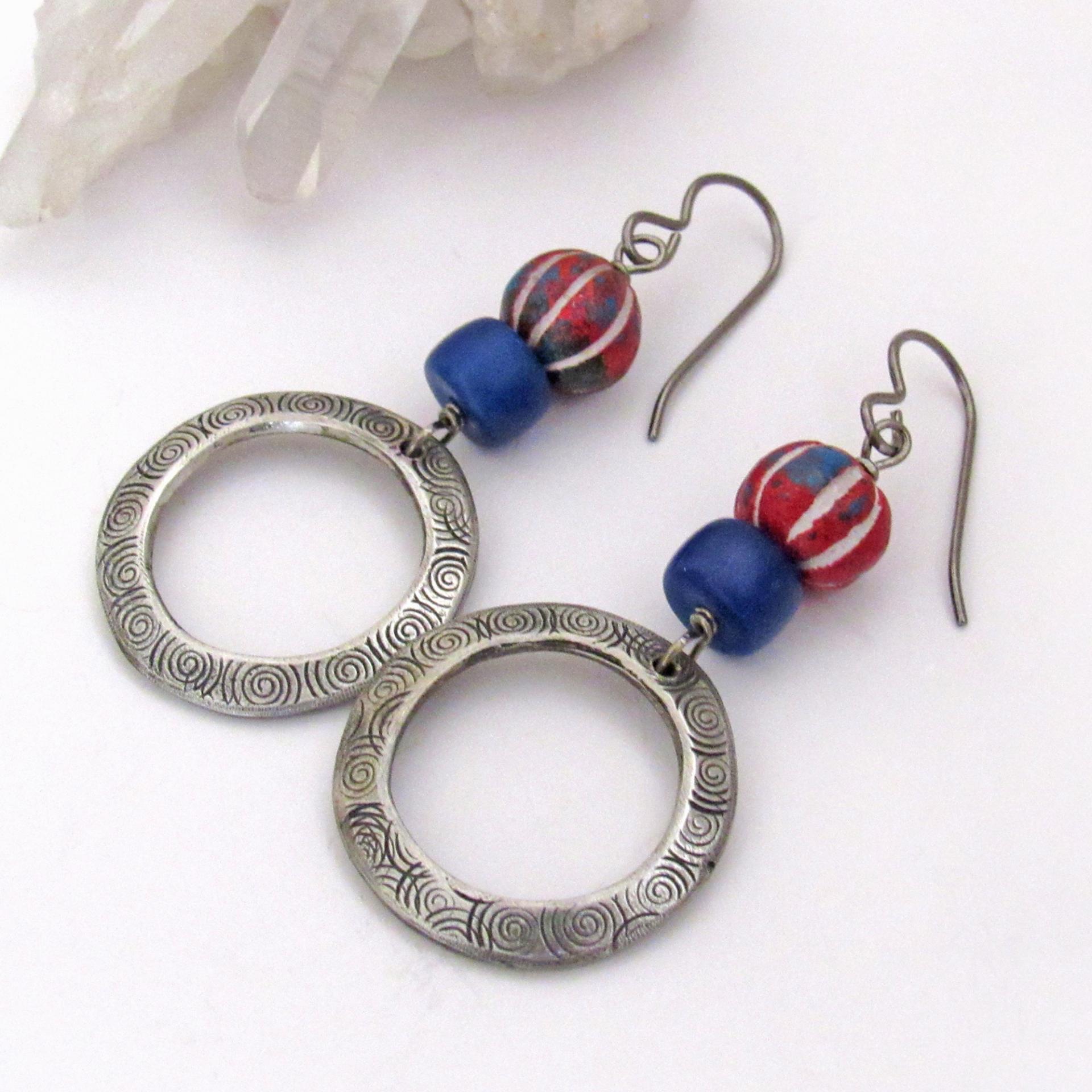 These handcrafted earrings feature silver pewter circle hoops with a hand stamped texture accented with red, white and blue carved clay beads and navy blue glass beads. They have an earthy, boho style and are lightweight and comfortable to wear. 