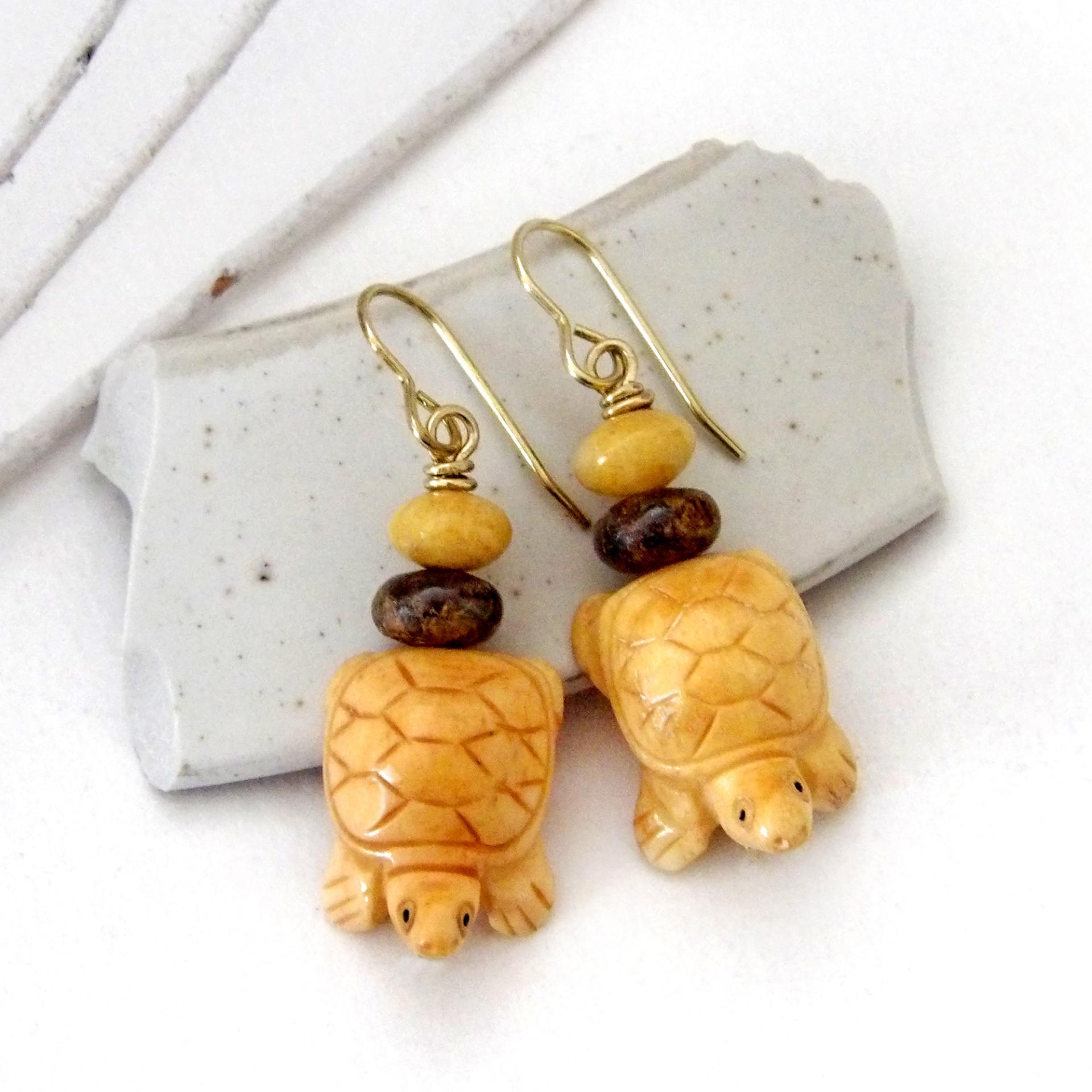 Super cute and fun to wear - these handmade earrings feature yellow jasper stones carved into sweet, little turtles. They are accented with fossilized beige coral and brown bronzite stone beads. They'll make a great gift for a turtle or animal lover. Turtles are powerful symbols of patience, wisdom, longevity and protection across many global cultures. Because of their hard shells and long lifespans, they represent stability and endurance, reminding us to move through life with steady determination.