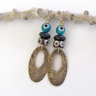 These handmade earrings feature gold brass hoops with a hand stamped texture accented with African batik bone beads and topped off with turquoise color evil eye glass and matte black glass beads.  Evil eye beads are protective amulets designed with concentric circles that mimic the appearance of a human eye. Beads with this symbolism have been used for thousands of years across different cultures to ward off bad luck, illness, or misfortune and push away the negative or envious energy of others.